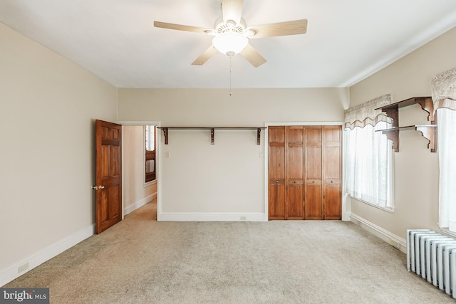 unfurnished bedroom featuring light colored carpet, ceiling fan, radiator, and a closet