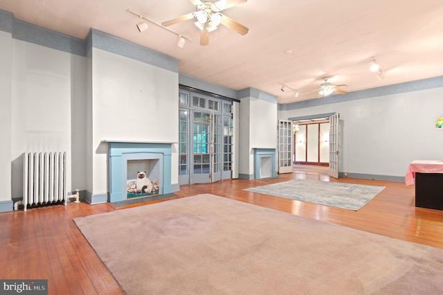 unfurnished living room with rail lighting, light hardwood / wood-style floors, radiator heating unit, and ceiling fan