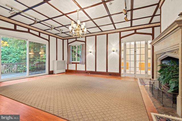 unfurnished living room featuring french doors, radiator heating unit, coffered ceiling, hardwood / wood-style flooring, and a chandelier