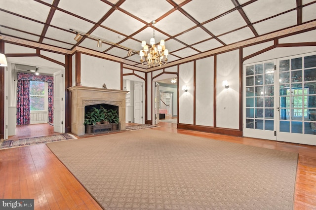 unfurnished living room with light hardwood / wood-style flooring, an inviting chandelier, coffered ceiling, and vaulted ceiling