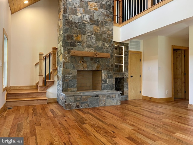 unfurnished living room featuring a stone fireplace, a high ceiling, and light hardwood / wood-style floors