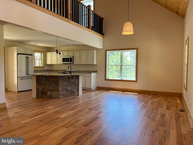 unfurnished living room featuring a towering ceiling, sink, and light hardwood / wood-style floors