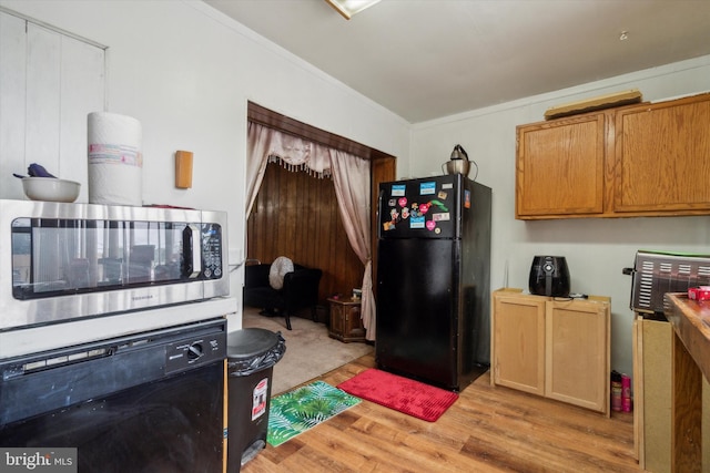 kitchen featuring wall oven, crown molding, light hardwood / wood-style flooring, and black fridge