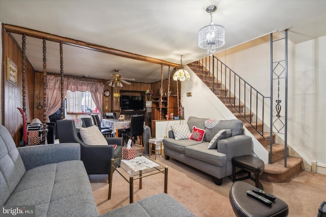 carpeted living room with beamed ceiling, wooden walls, and ceiling fan with notable chandelier