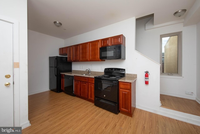 kitchen with sink, light wood-type flooring, black appliances, and light stone countertops