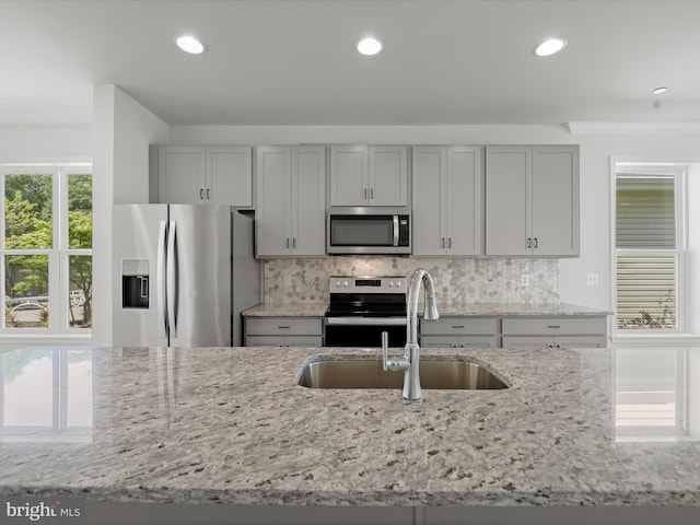 kitchen with light stone countertops, backsplash, gray cabinets, stainless steel appliances, and sink