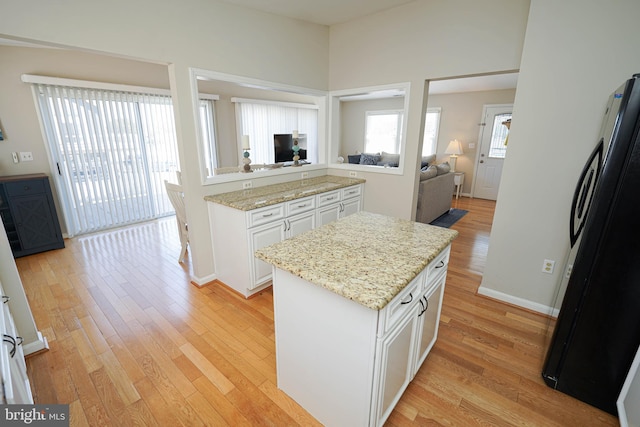 kitchen with light stone countertops, light wood-type flooring, fridge, and white cabinetry