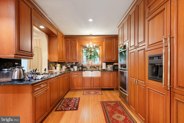 kitchen featuring sink, an inviting chandelier, light hardwood / wood-style flooring, backsplash, and decorative light fixtures