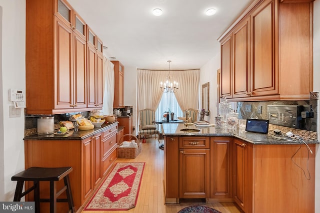 kitchen with kitchen peninsula, light hardwood / wood-style flooring, dark stone counters, and decorative light fixtures