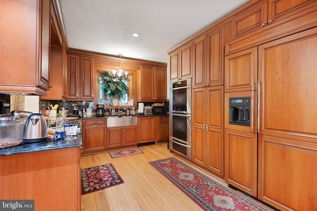 kitchen with sink, hanging light fixtures, double oven, dark stone counters, and light hardwood / wood-style floors