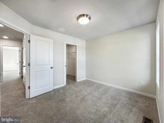 unfurnished bedroom with a textured ceiling, a spacious closet, carpet floors, and a closet