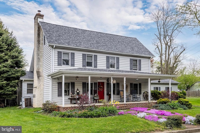 view of front of home with a front yard, central AC unit, and covered porch