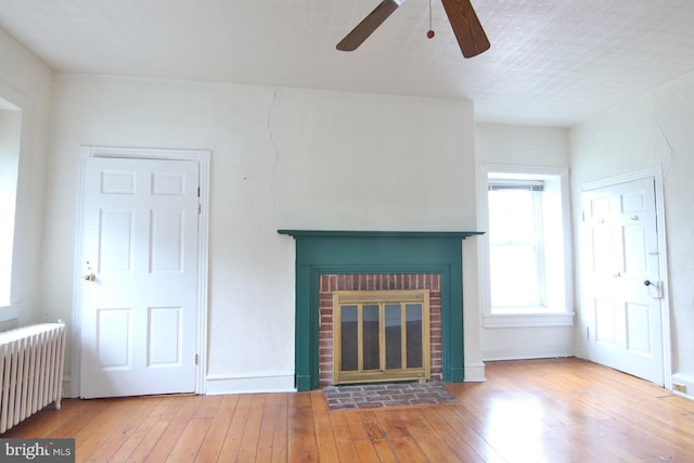 unfurnished living room featuring a fireplace, ceiling fan, light hardwood / wood-style floors, and radiator heating unit