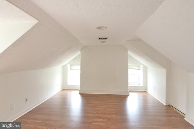 additional living space with lofted ceiling, wood-type flooring, and a textured ceiling