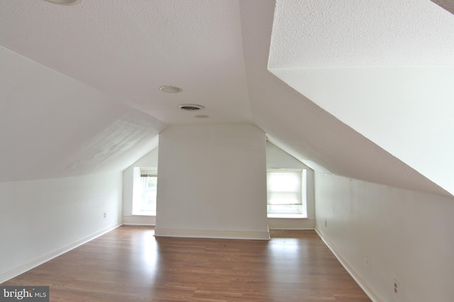 additional living space with dark hardwood / wood-style flooring, a textured ceiling, and lofted ceiling