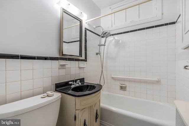 full bathroom with tile walls, toilet, large vanity, and tiled shower / bath combo