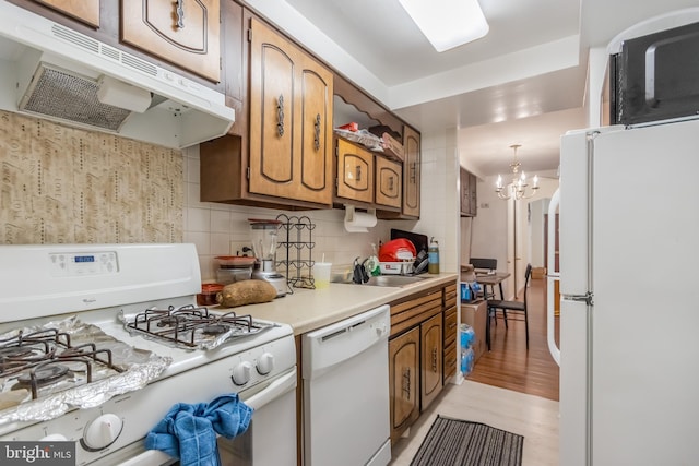 kitchen with pendant lighting, white appliances, light hardwood / wood-style flooring, a notable chandelier, and tasteful backsplash