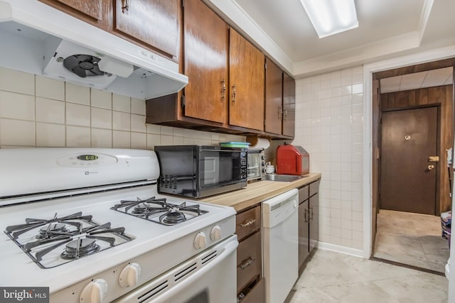 kitchen with tile walls, white appliances, sink, and light tile floors