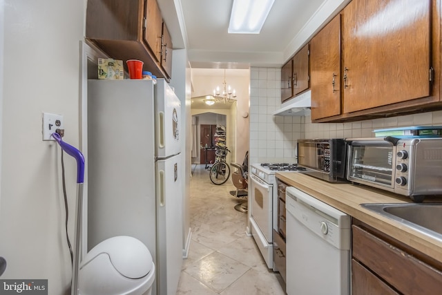 kitchen with light tile floors, white appliances, backsplash, custom range hood, and an inviting chandelier