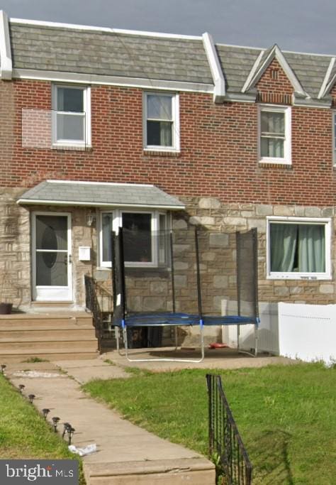 rear view of property featuring a trampoline and a yard