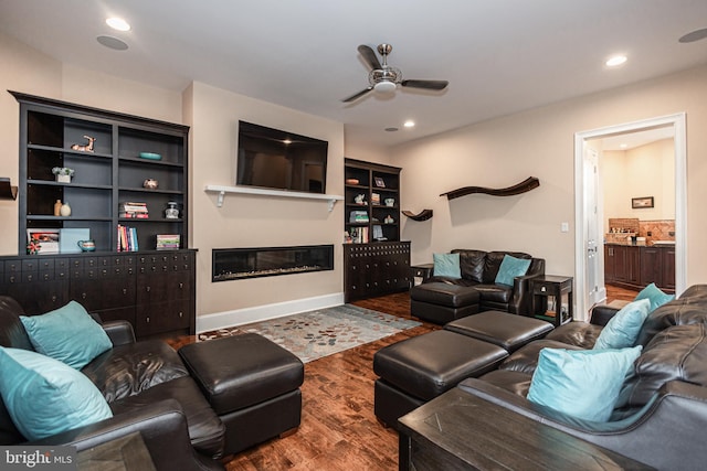 living area with recessed lighting, a ceiling fan, wood finished floors, and a glass covered fireplace