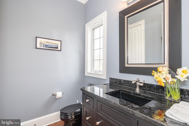 half bathroom featuring toilet, vanity, and baseboards