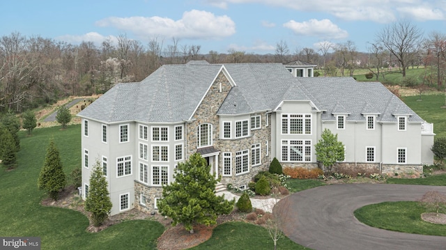 view of front facade featuring driveway, stone siding, stucco siding, and a front yard