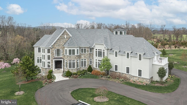 view of front of property with stone siding, curved driveway, a front lawn, and stucco siding