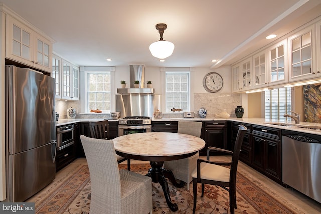 kitchen with decorative light fixtures, stainless steel appliances, tasteful backsplash, wall chimney exhaust hood, and sink