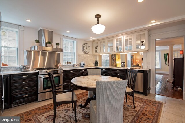 kitchen with wall chimney exhaust hood, a healthy amount of sunlight, hanging light fixtures, light tile flooring, and appliances with stainless steel finishes