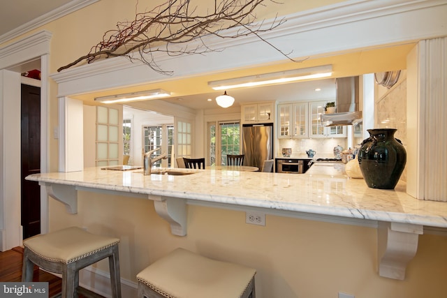 kitchen with decorative light fixtures, a breakfast bar, stainless steel refrigerator, light stone counters, and tasteful backsplash