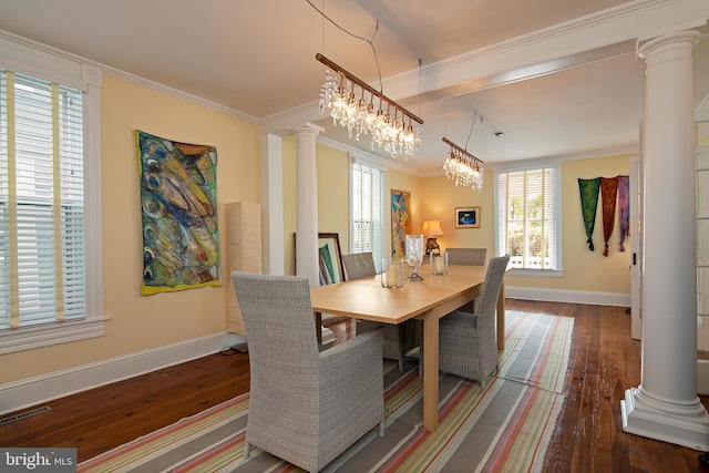 dining room with hardwood / wood-style floors, crown molding, an inviting chandelier, and decorative columns