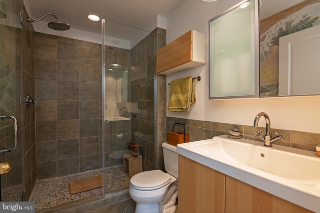 bathroom with walk in shower, vanity, toilet, and tile walls