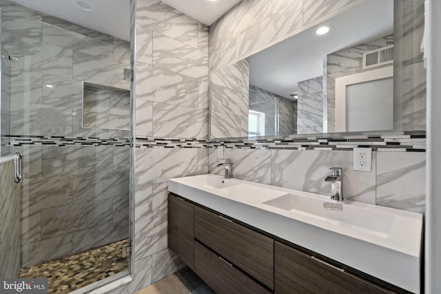 bathroom with tile walls, double sink, large vanity, and a shower with shower door