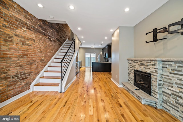 staircase featuring brick wall, light hardwood / wood-style flooring, and a fireplace