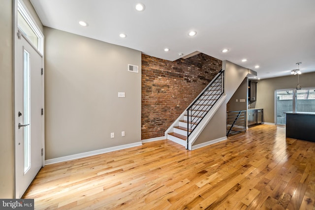 entryway with brick wall and light hardwood / wood-style floors