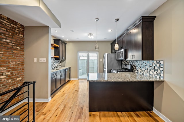 kitchen featuring tasteful backsplash, hanging light fixtures, brick wall, stainless steel appliances, and light hardwood / wood-style flooring