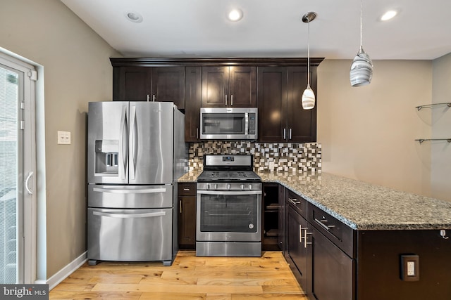 kitchen with hanging light fixtures, light wood-type flooring, appliances with stainless steel finishes, light stone counters, and tasteful backsplash