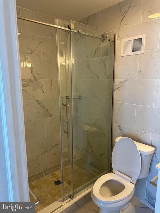 bathroom with tile walls, a shower with shower door, toilet, and tile flooring