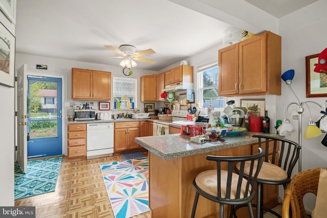 kitchen with kitchen peninsula, a kitchen bar, white appliances, ceiling fan, and light parquet flooring