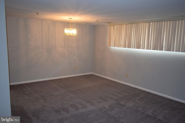 spare room with a chandelier and dark colored carpet