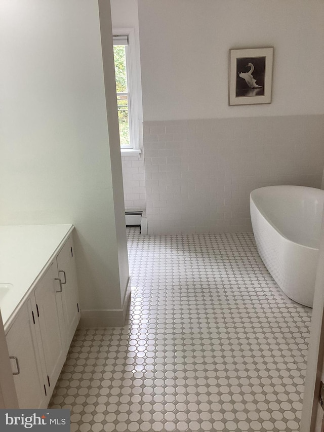 bathroom with a baseboard radiator, a bath, vanity, and tile walls