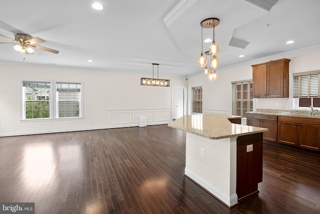 kitchen featuring pendant lighting, ceiling fan, light stone countertops, a center island, and ornamental molding