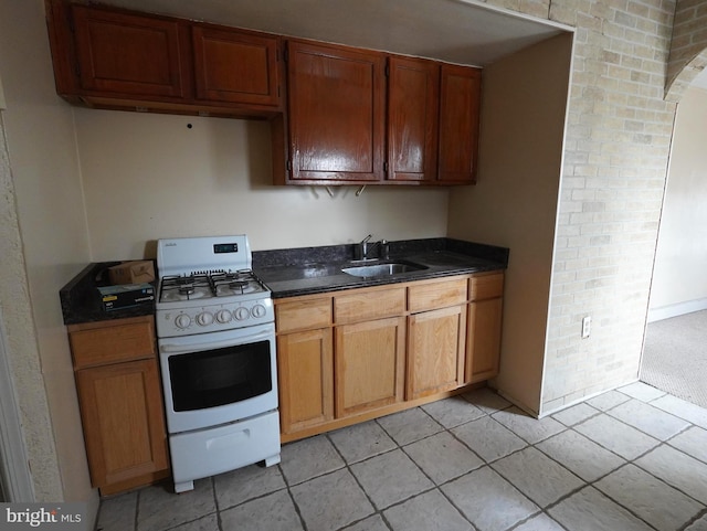 kitchen featuring white gas range, brick wall, light tile floors, and sink