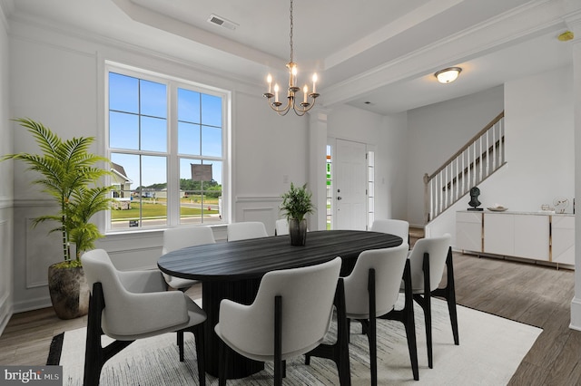 dining space with a chandelier, dark hardwood / wood-style floors, a raised ceiling, and ornamental molding