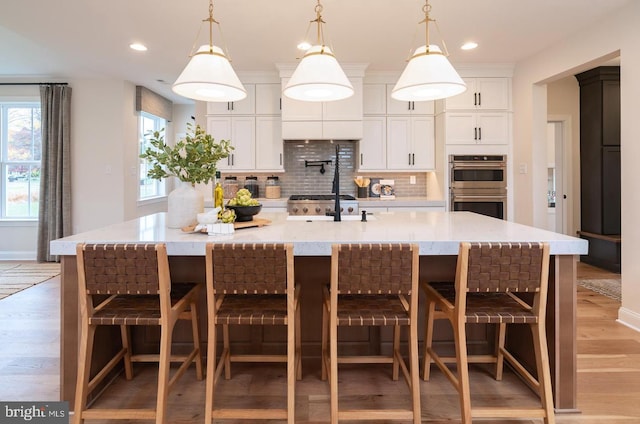 kitchen with a kitchen bar, a center island with sink, double oven, and pendant lighting