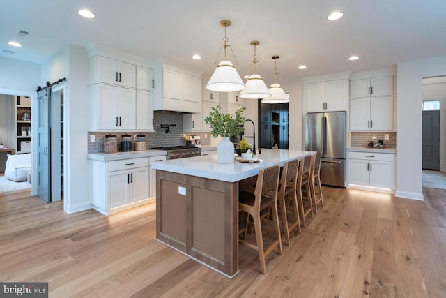 kitchen featuring a barn door, light wood-type flooring, high end fridge, an island with sink, and pendant lighting