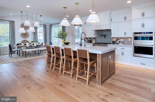 kitchen featuring appliances with stainless steel finishes, light wood-type flooring, white cabinetry, and an island with sink