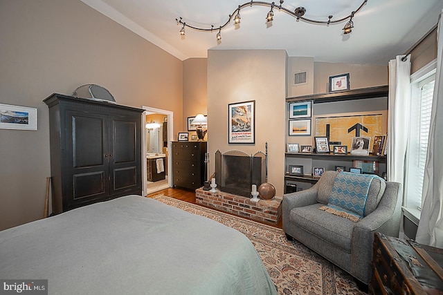 bedroom with rail lighting, lofted ceiling, a fireplace, and dark wood-type flooring