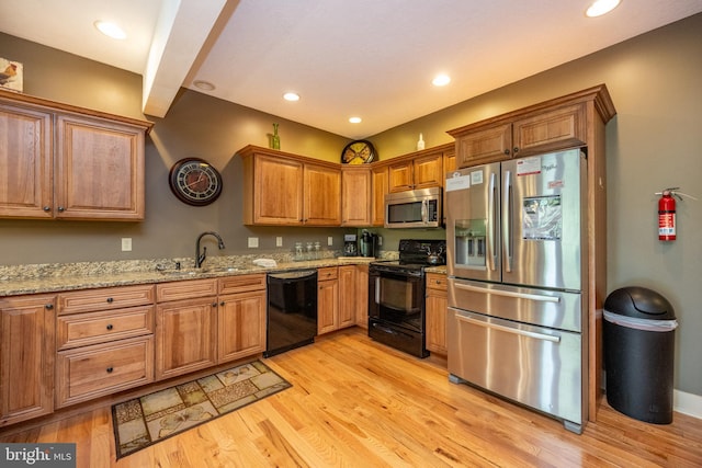 kitchen with light hardwood / wood-style floors, black appliances, sink, and light stone countertops